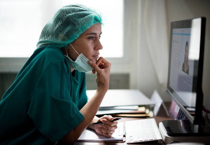 A healthcare worker in green scrubs and a hairnet reviewing information on a computer screen.