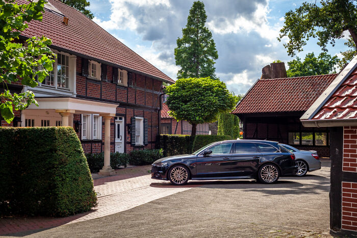 A dark station wagon car parked outside a traditional brick house like obvious lies.