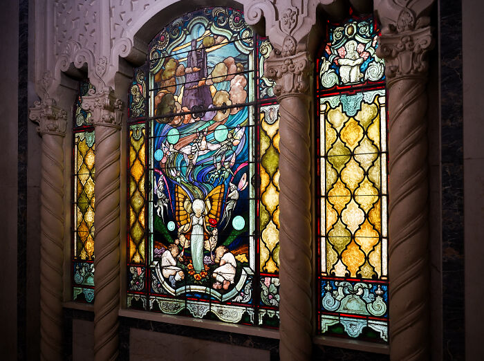 Intricate stained glass window with angelic figures and vibrant colors framed by ornate columns Intricate stained glass window with angelic figures and vibrant colors framed by ornate columns
