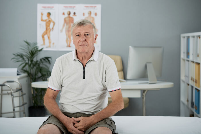An older male patient sits on an examination table in a healthcare clinic.