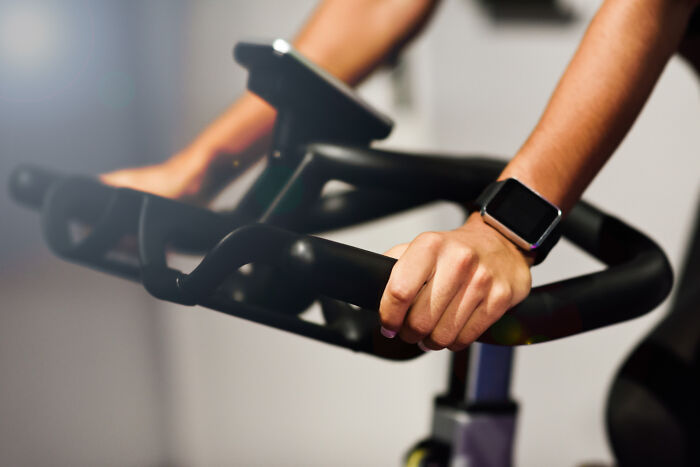A person riding a stationary exercise bike with a smartwatch, showing obvious lies about fitness routines.