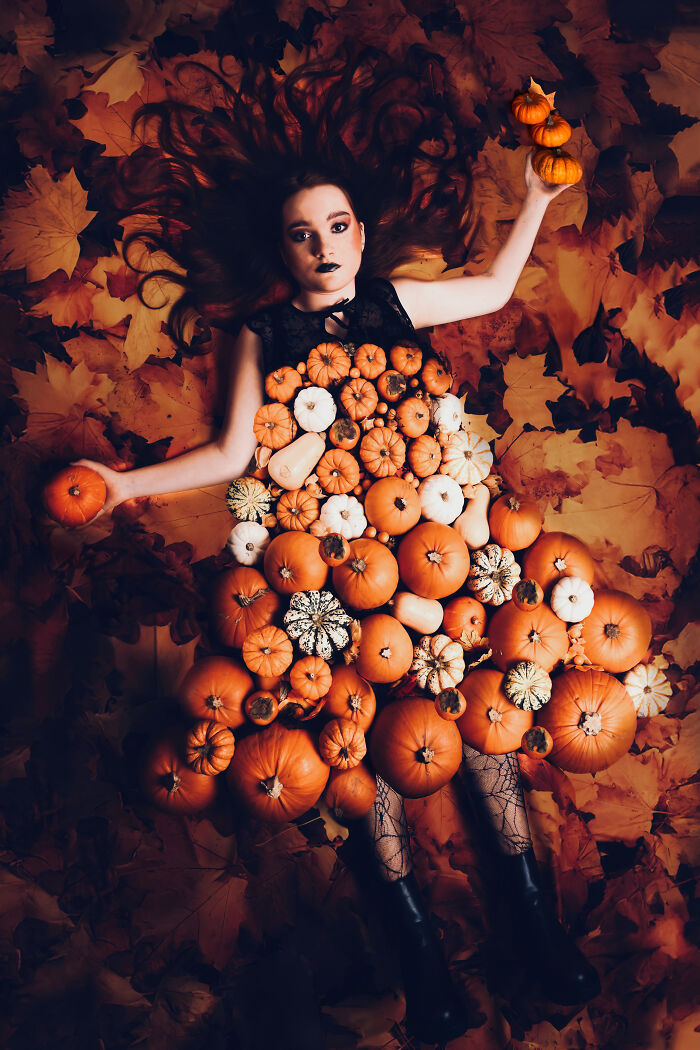 Woman wearing a dress made of miniature pumpkins lying dramatically on a bed of autumn leaves.