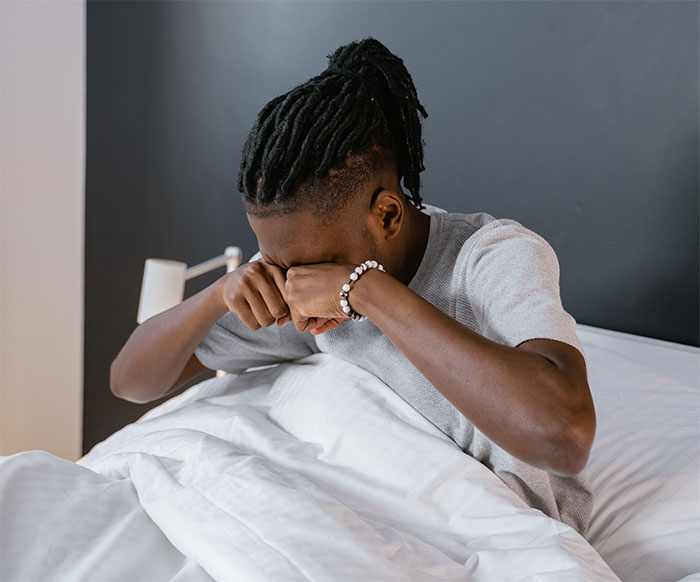 Man rubbing eyes in bed indicating eye discomfort Man rubbing eyes in bed indicating eye discomfort