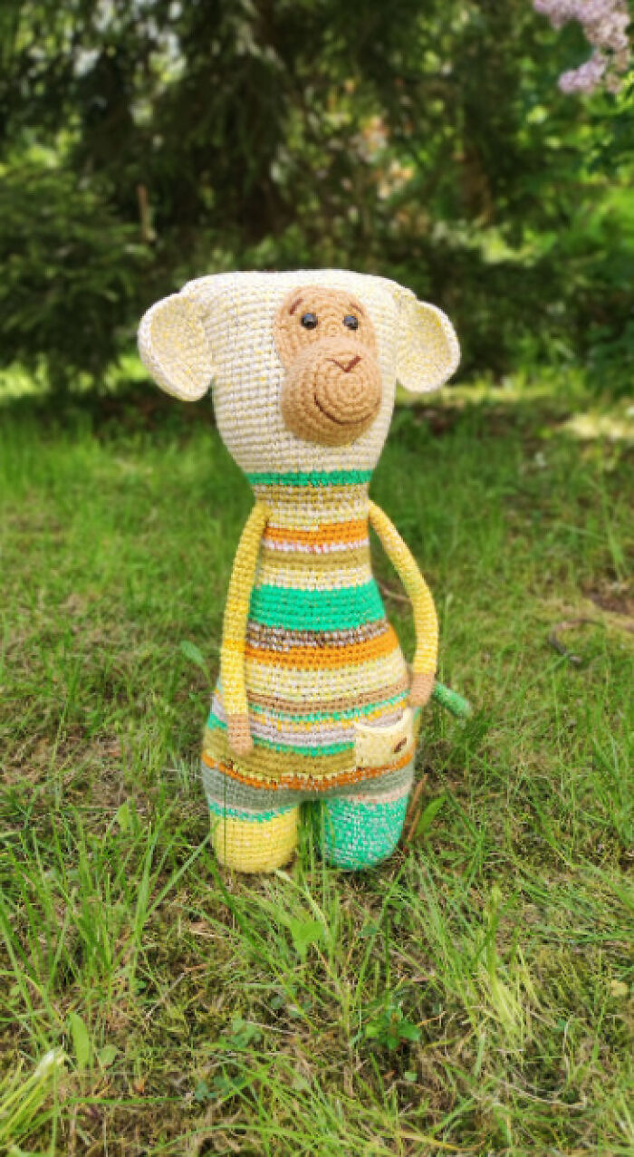 A cute monkey crochet creature with colorful stripes standing upright on a green lawn with a blurred background
