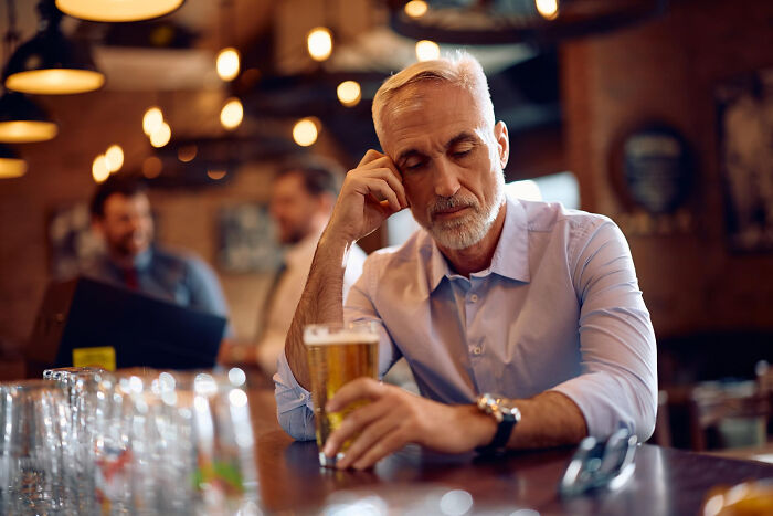 Sad man sitting alone in bar with a glass of beer in front of him