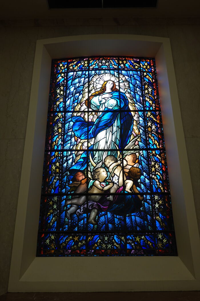 Detailed stained glass window showing a robed figure surrounded by cherubs and stars Detailed stained glass window showing a robed figure surrounded by cherubs and stars