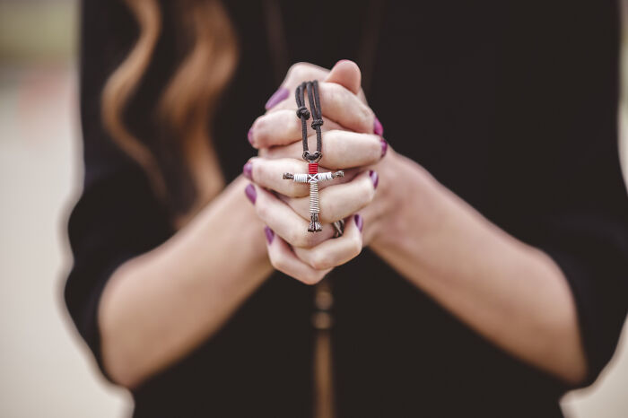 Close-up of hands clasped in prayer holding a cross necklace, referencing lesser-known cults.