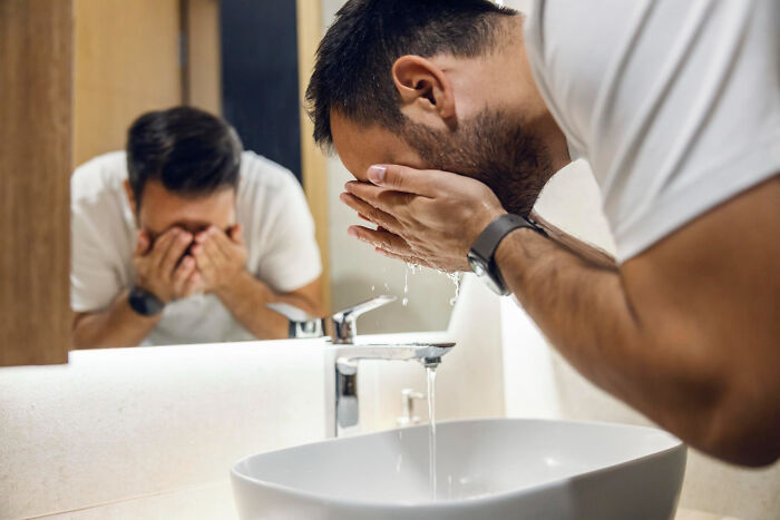 A man washing his face in a bathroom mirror, representing candid thoughts doctors and nurses have about hygiene