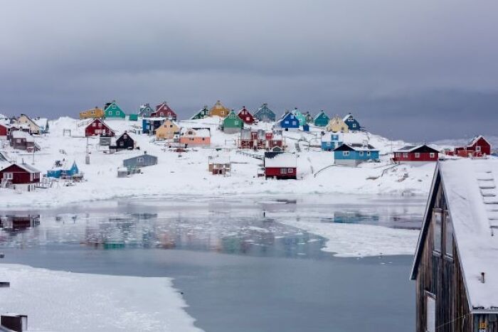 Colorful houses clustered on snowy hillside by frozen water