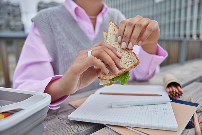 A woman holding a sandwich outdoors while having her lunch break