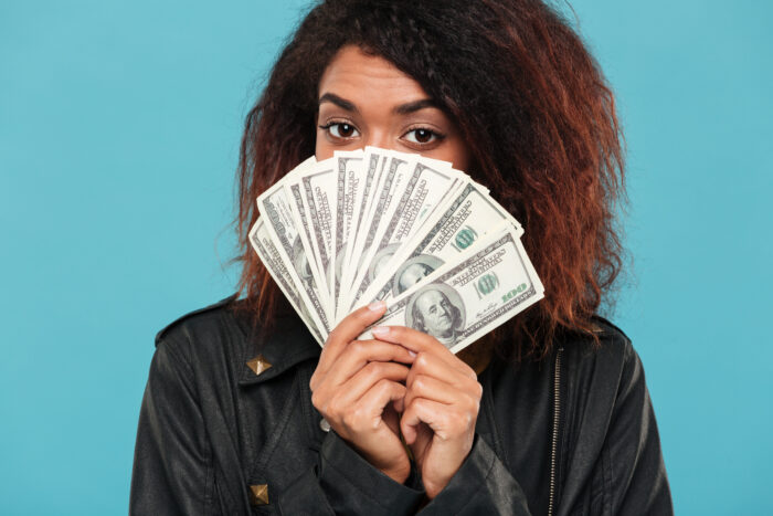 A young woman covering her face with a fan of cash after finding money in her bank account. A young woman covering her face with a fan of cash after finding money in her bank account.