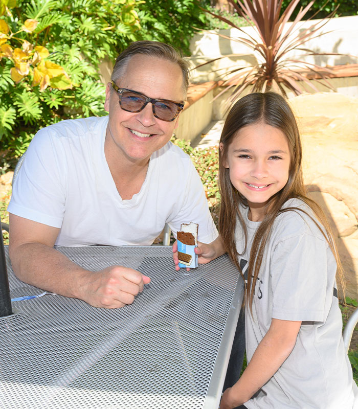 Chad Lowe smiles alongside his young daughter Fiona Lowe as she holds an ice cream sandwich.