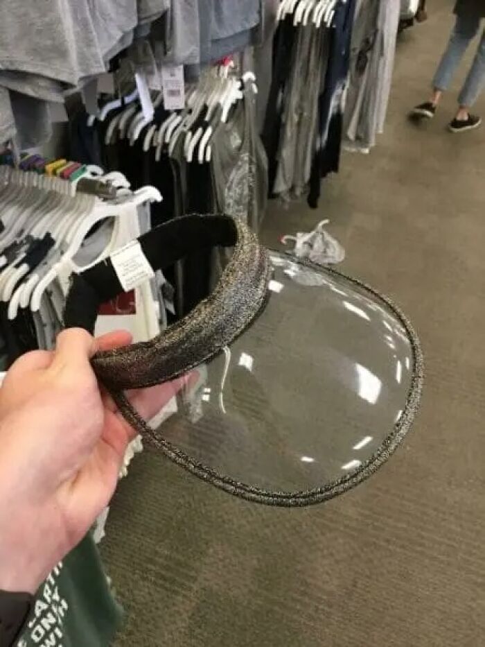 Transparent face shield held in a store aisle with clothing racks behind