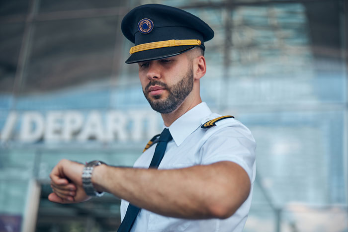 Airline pilot in uniform checking his wristwatch, symbolizing busy lives and divorce stories.