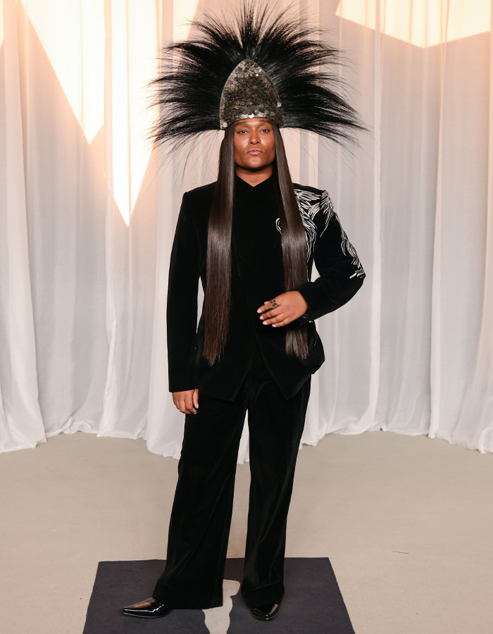 Celebrity wearing a black suit with an elaborate feathered headpiece at the Academy Museum Gala