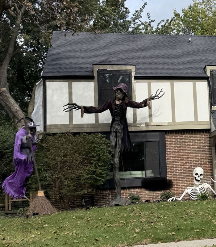 Spooky Halloween decoration in a front yard including a tall scarecrow figure and skeleton.