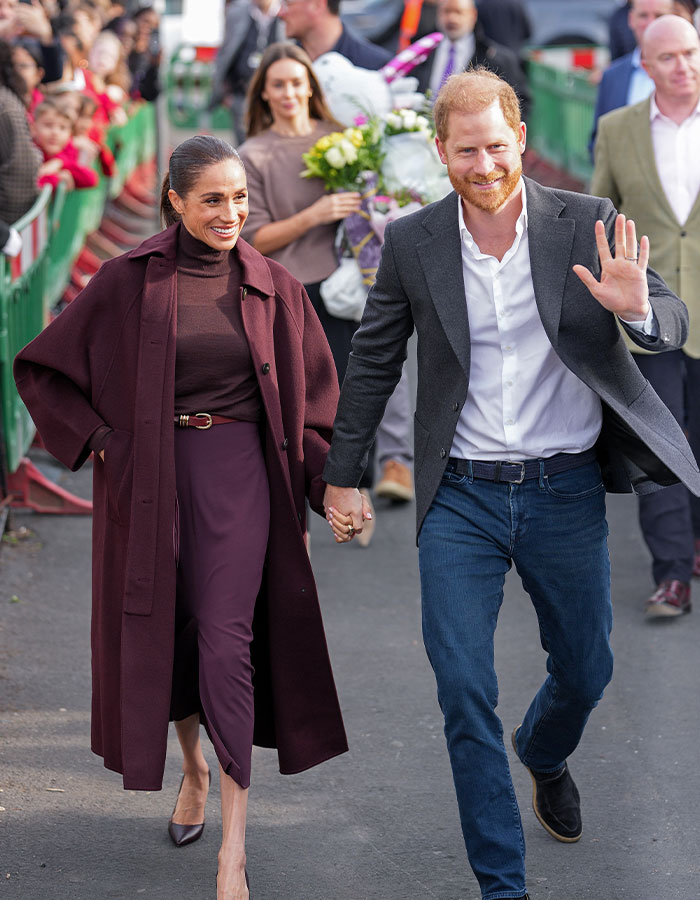 Meghan Markle and Prince Harry walking together during a food bank visit while greeting people.