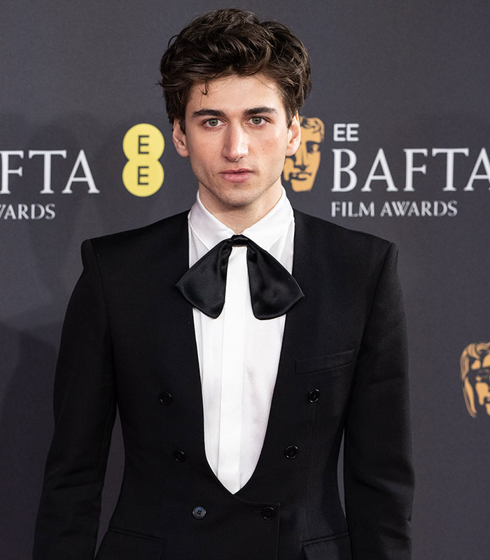 Hollywood star Sebastian Croft posing in a black suit with a large bow tie.