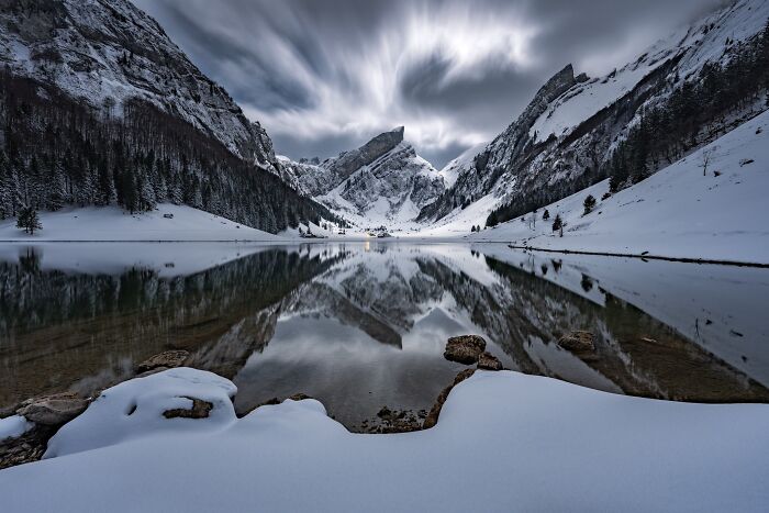 Natural landscape photography of dramatic snow-capped mountains reflecting off a serene alpine lake.