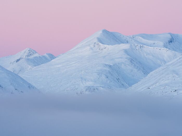 Snowy mountain peaks glowing under a soft pink sky in a natural landscape photograph.