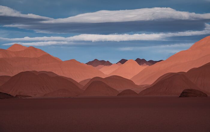 Rolling red sand dunes under a blue sky with soft white clouds in landscape photography