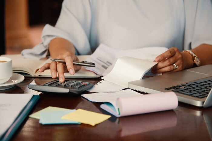 Hands using a calculator near documents and a laptop to calculate finances after obvious lies.