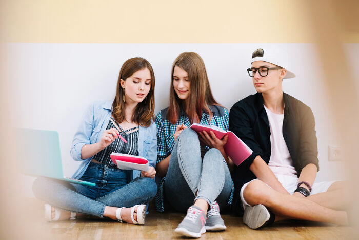 Three young students sitting on the floor studying together, highlighting the collaborative efforts of students.