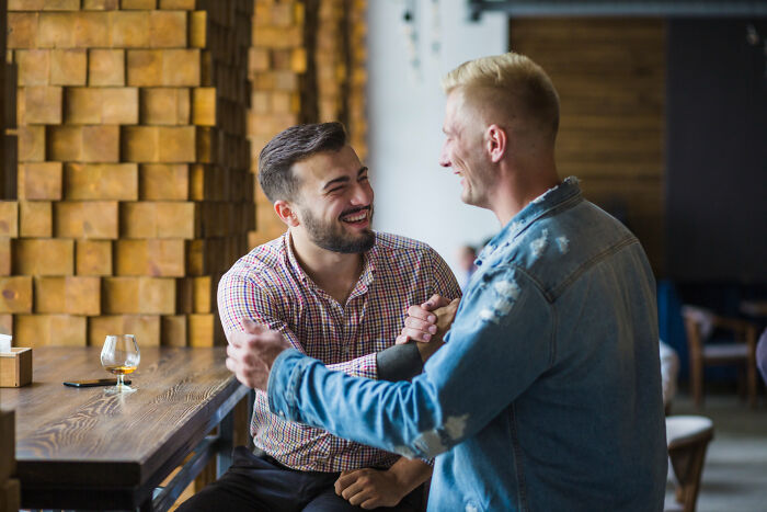 Two men smiling and arm-wrestling at a table, recalling personal divorce stories.