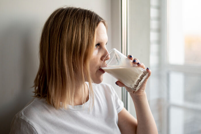 Woman drinking glass of milk by window in humorous revenge story setting