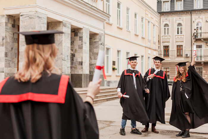 Students wearing graduation gowns celebrating with their diplomas outside the university building