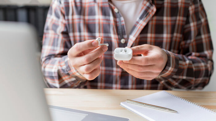 Hands holding wireless earbuds and charging case on desk