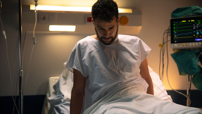 A male patient sitting up in a hospital bed with an IV drip, monitored by diligent healthcare workers