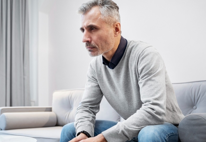 Middle-aged man sitting thoughtfully on a couch in a living room.