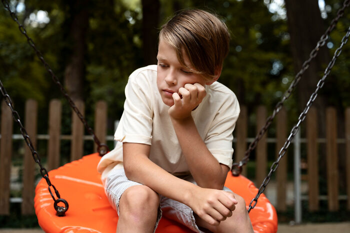 A sad boy sitting on a playground swing amidst family divorce stories.