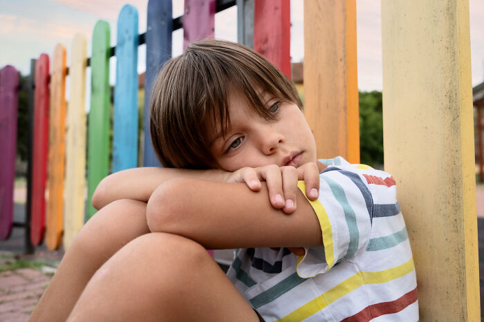 Sad boy sitting alone near colorful fence illustrating being disowned by their families