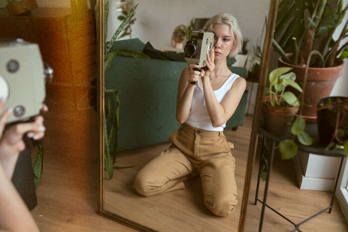 A woman filming herself in a mirror with a vintage camera, capturing obvious lies about her hobby.
