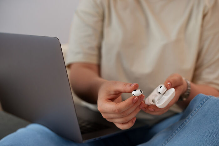 Person holding wireless earbuds near laptop showing unhinged things to get back at ex