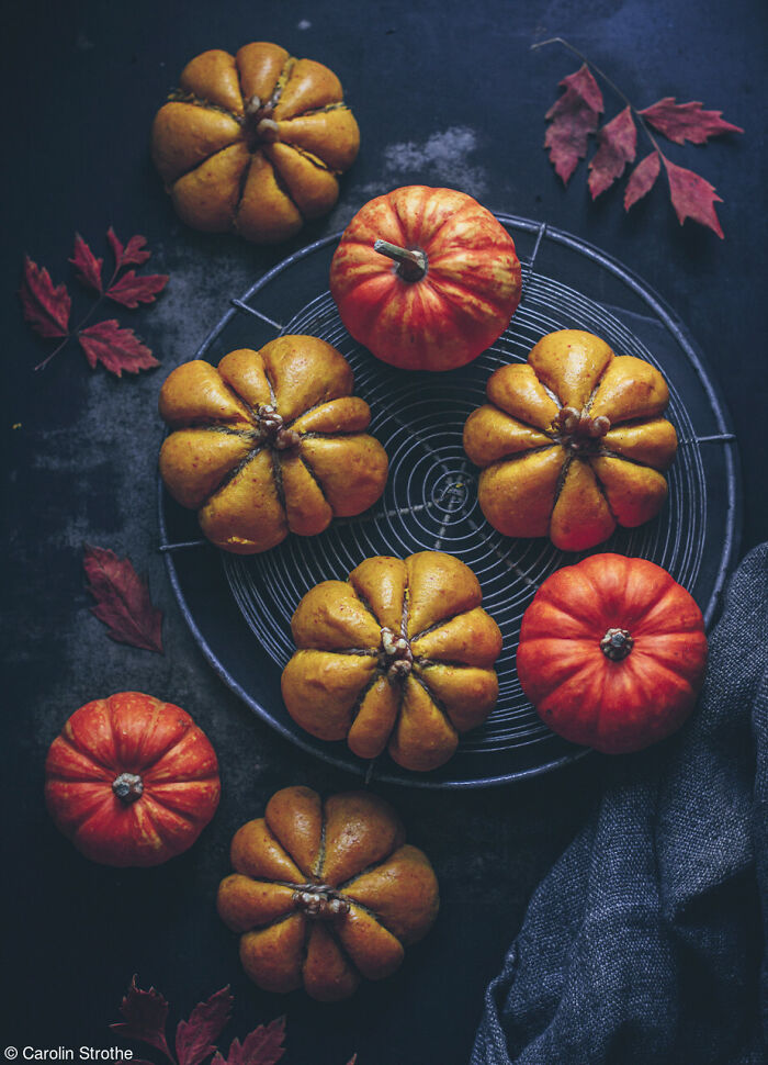 Artistic arrangement of mini pumpkin rolls and small real pumpkins served on a round wire rack.