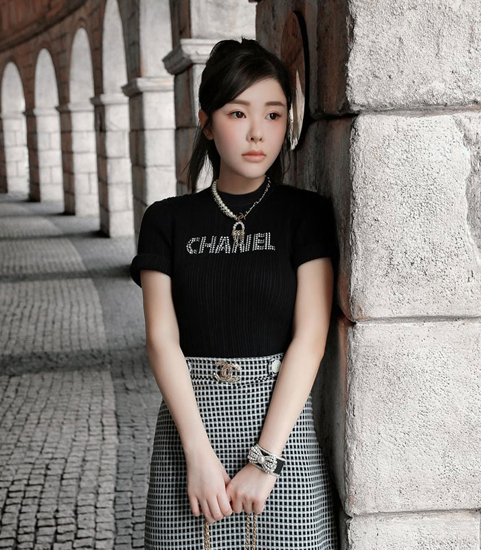 Woman standing by stone pillar wearing black Chanel top and checkered skirt Woman standing by stone pillar wearing black Chanel top and checkered skirt