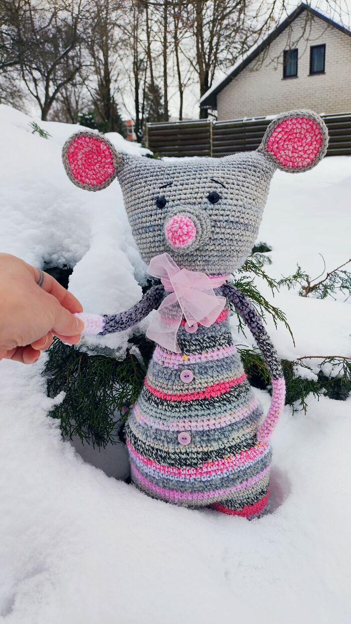 A mouse crochet creature with pink ears standing in the snow.