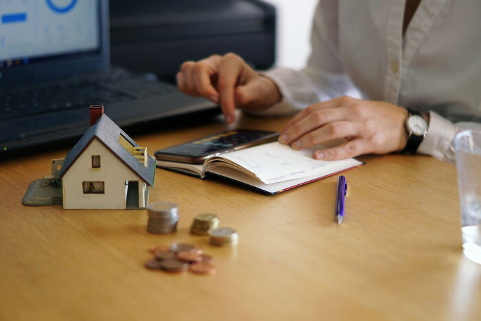 Hands calculating finances with a model house on a desk, representing division of property in divorce stories.