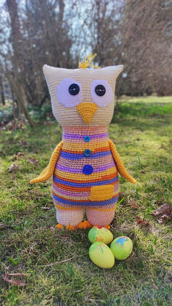 An owl crochet creature standing in a grassy field with decorative eggs.