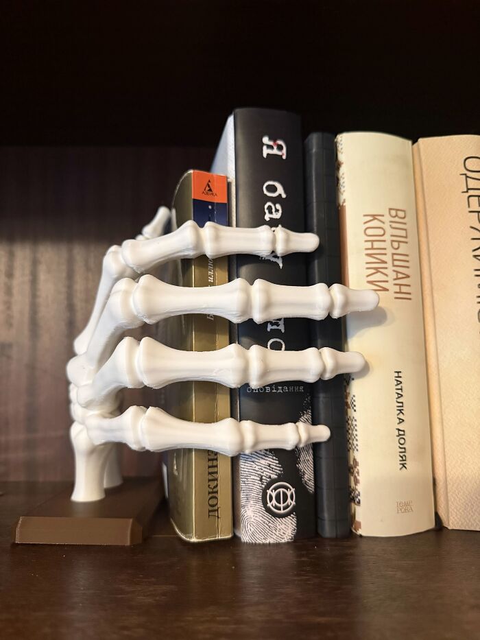A skeleton hand bookend among 3D prints on a bookshelf