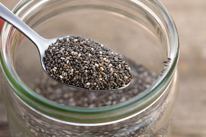 Spoonful of chia seeds over glass jar filled with seeds