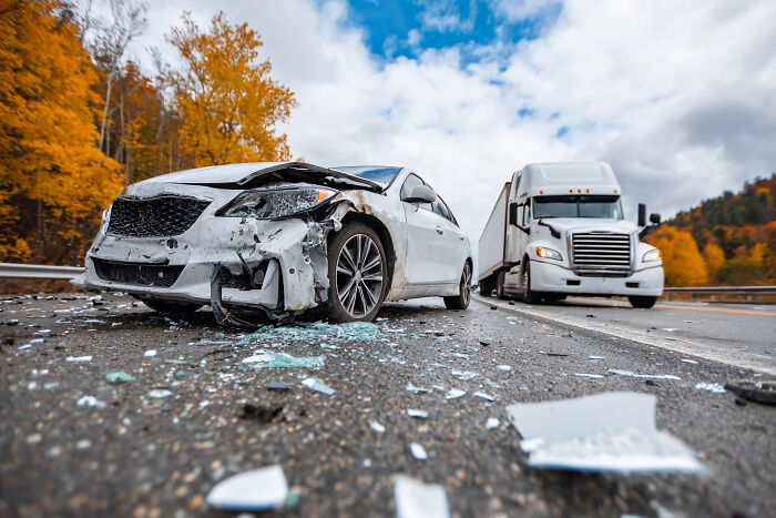 Damaged white car after accident with truck and debris on road in autumn
