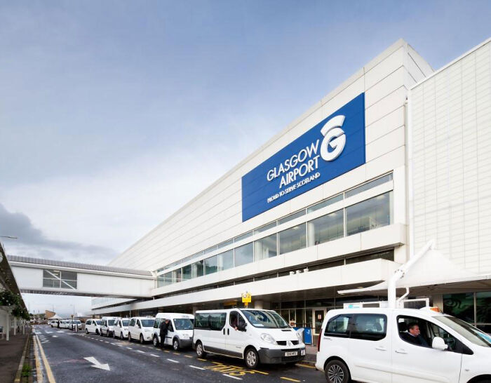 Exterior view of the Glasgow Airport terminal entrance with white taxis parked along the curb.