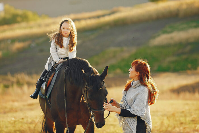 Child riding a horse with adult supervisor in outdoor horse riding scene