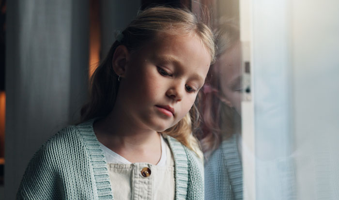 Sad young girl looking out of a window after learning about her mother's secret affair Sad young girl looking out of a window after learning about her mother's secret affair