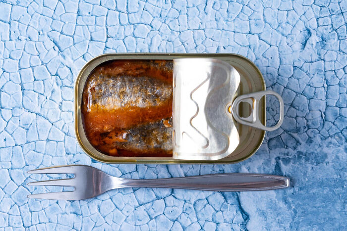 Open can of sardines with fork on textured blue surface for hilarious revenge