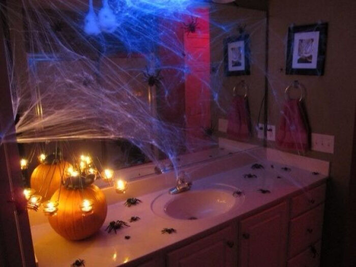 Bathroom decorated with cobwebs, fake spiders, and glowing pumpkins for Halloween.